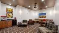 Located in Aurora, CO, this purpose-built home theater room offers a well-designed cinematic experience in a compact, single-floor layout. The room is anchored by a large wall-mounted projection screen at one end, paired with a ceiling-mounted projector, creating an immersive viewing setup. In-wall surround sound speakers are strategically positioned throughout, ensuring high-quality audio from every seat in the room.

The seating arrangement is both generous and inviting, centered around a large L-shaped sectional sofa in warm earth tones, complemented by several plaid and upholstered accent chairs. A rustic wooden side table serves as a centerpiece. A bold Hollywood-themed canvas painting adorns the wall above the sectional, lending a playful nod to classic cinema culture.

The room's aesthetic is defined by its rich, dark ceiling contrasted against crisp white walls, with recessed lighting and elegant vertical wall sconces providing a warm, ambient glow. A geometric-patterned carpet in muted blues, browns, and taupes adds texture underfoot. A built-in cabinet near the screen houses a popcorn machine, completing the authentic movie-night experience. Warm wood trim detailing and a solid wood door add refined, traditional character to the space.