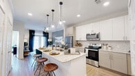 This thoughtfully designed single-floor residence offers an efficient yet comfortable layout that maximizes every square foot. The open-concept kitchen and living area serves as the heart of the home, anchored by a striking granite-topped island with bar seating and elegant pendant lighting overhead. Crisp white cabinetry, a classic tile backsplash, and a full suite of stainless steel appliances — including a refrigerator, range, and microwave — complete the kitchen. Light wood-style flooring flows throughout, lending warmth and cohesion to the space.

The living area is bathed in natural light from large windows dressed with stylish curtains, creating a bright and welcoming atmosphere. A pantry and utility room add practical functionality, while a dedicated laundry area enhances everyday convenience.

The bedroom is a serene retreat, featuring large windows with ample natural light, a ceiling fan, and direct access to a walk-in closet with built-in shelving and hanging rods. Two additional closets throughout the unit provide generous storage. The bathroom is elegantly finished with a granite-topped vanity, a large framed mirror, wood-toned cabinetry, and a tub-shower combination adorned with marble-style tile. A private patio rounds out the space, offering a welcome outdoor retreat.
