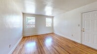 Located at 6415 Newport Ave in Norfolk, Virginia, this 2-bedroom, 1-bathroom single-story home offers a practical and well-organized floor plan. Warm hardwood flooring flows throughout the living room and both bedrooms, lending a classic character to the interiors. The living room is bright and open, featuring a paneled entry door and natural light that highlights the polished wood floors.

The kitchen is equipped with warm oak cabinetry, light granite-style countertops, a double-basin sink, and white appliances including a freestanding range and refrigerator. A window brings in natural light, and light-toned flooring contrasts neatly with the wood cabinetry. The kitchen opens directly to the living area, creating an easy flow between spaces.

Both bedrooms feature the same rich hardwood floors and are filled with natural light from multiple windows that offer views of surrounding greenery. The primary bedroom is comfortably sized, while the second bedroom provides a versatile space suitable for various uses.

The bathroom showcases a classic mid-century aesthetic with cream and black wall tile, a full bathtub with shower, and a window that provides ventilation and natural light. Wood-look flooring grounds the space. A connecting hallway ties all rooms together efficiently, completing this straightforward and functional home.