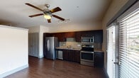 This single-floor residence is designed with a practical, modern aesthetic throughout. The open kitchen serves as a central feature, outfitted with a full suite of stainless steel appliances including a refrigerator, electric range with oven, built-in microwave, and dishwasher. Rich, dark espresso-toned cabinetry provides generous storage above and below the countertops, which are finished in a warm stone-look surface. A mosaic tile backsplash in neutral earth tones adds visual texture between the upper and lower cabinets. A ceiling fan with an integrated light kit and a track lighting fixture illuminate the main living and kitchen area, which is finished with warm wood-look plank flooring that extends throughout the space.

A set of French doors opens to a private balcony, allowing natural light to fill the interior and offering an outdoor connection. A hallway leads to the additional rooms and includes built-in open shelving, providing convenient storage. The bathroom features a full tub-and-shower combination with tile surround, a granite-top vanity, and a large mirror. The layout is completed by closeted storage and additional utility spaces, making the overall design both functional and cohesive.