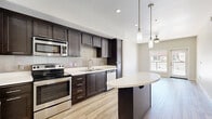 Located at 450 Tenth Avenue in San Diego's vibrant 92101 neighborhood, this well-appointed one-bedroom, one-bathroom residence offers a thoughtfully designed single-floor layout. Light wood-tone flooring flows throughout, complementing the clean white walls and creating a bright, cohesive aesthetic.

The open-concept living area seamlessly integrates the kitchen, dining, and living spaces. The kitchen is a standout feature, showcasing rich dark-stained cabinetry with modern hardware, crisp white quartz countertops, a tile backsplash, and a full suite of stainless steel appliances including a refrigerator, electric range, microwave, and dishwasher. A curved kitchen island provides additional prep space and casual seating, while pendant lighting above adds a refined touch.

A hallway connects the living areas to the private bedroom, which offers a comfortable footprint with two closets — one of which is a generously sized walk-in with built-in shelving and hanging rods. The bathroom is finished with large-format tile flooring, a tiled tub-shower combination, and a dark-cabineted vanity with a white countertop.

Additional features include an in-unit laundry area and a private balcony with metal rail detailing that opens to views of the surrounding San Diego skyline and urban landscape.