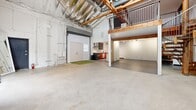 Located at 2888 E Walnut St in Pasadena, CA, this distinctive two-floor live-work loft offers an industrial-chic aesthetic defined by soaring ceilings, exposed wood beams, and visible ductwork that lend the space a raw, creative character. The expansive main floor features polished concrete floors, white-painted walls, and generous natural light streaming through large windows, creating a bright and versatile open-plan layout that accommodates a living area, dining space, and a compact kitchen with dark cabinetry and stainless appliances. A large roll-up garage door adds to the industrial feel while providing an option for indoor-outdoor connectivity. A striking spiral staircase with warm wood treads leads to the upper mezzanine level, which is finished with rich hardwood flooring and framed by metal railings. This upper level serves as the primary bedroom retreat, offering an intimate and elevated vantage point over the main floor, with exposed timber trusses overhead. Two bathrooms feature dark tile flooring, tub-shower combinations with mosaic tile accents, and modern vanities with sleek fixtures. A dedicated closet completes the functional layout. The overall ambiance blends industrial warehouse origins with residential warmth, making it a compelling space for creative professionals or those seeking a one-of-a-kind urban dwelling in the heart of Pasadena.