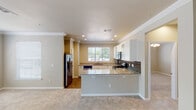 Located in Grapevine, Texas, this single-story residence offers a well-designed, open-concept layout that connects the kitchen and living areas seamlessly. The kitchen is a standout feature, showcasing granite countertops, white shaker-style cabinetry with glass-front upper panels, a gray subway tile backsplash, and a full suite of stainless steel appliances including a range, over-the-range microwave, dishwasher, and refrigerator. A peninsula with matching granite provides additional counter space and a natural division between the kitchen and the carpeted living area. Natural light filters in through multiple windows fitted with blinds, brightening the neutral-toned interior walls accented by crisp crown molding throughout. The living area is generously proportioned with plush carpet underfoot and a ceiling fan overhead. Bedrooms are carpeted and offer ample space, with six-panel doors and easy hallway access. The bathroom features a granite-topped vanity with white cabinetry, wood-look flooring, a tub-shower combination, and a built-in linen cabinet for added storage. Rich wood-look flooring runs through the kitchen and bathrooms, complementing the warm, cohesive aesthetic of the home.