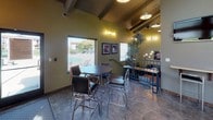 Located at 923 E Sitka Ave in Spokane, WA, this single-floor space offers a well-designed interior that balances bold aesthetics with functional living. The kitchen is a standout area, featuring rich dark wood cabinetry, stainless steel appliances including a refrigerator, microwave, and range, a mosaic tile backsplash, and warm terracotta-orange accent walls that lend an inviting, energetic character to the space. The flooring throughout carries a durable stone-tile appearance that ties the rooms together cohesively. The living area is defined by soaring ceilings with generous vertical windows that allow natural light to pour in. A floor-to-ceiling tile-surround fireplace serves as a dramatic focal point, complemented by dark hardwood flooring and a cozy seating arrangement. The dining area showcases exposed wooden beam ceilings that add architectural texture, alongside pendant and accent lighting that creates a warm ambiance. Multiple windows provide views of the surrounding neighborhood, keeping the space feeling open and connected to the outdoors. The layout flows naturally between the kitchen, living, and dining zones, making the space versatile and well-suited for both everyday use and entertaining. Overall, the space presents a bold, contemporary design highlighted by rich color contrasts, architectural detailing, and thoughtful lighting throughout.