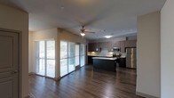 This two-story, 2-bedroom, 2-bathroom townhouse delivers a well-designed living experience across two thoughtfully laid-out floors. The main level features an open-concept floor plan that seamlessly connects the living area to the kitchen, creating a bright and functional space ideal for both everyday living and entertaining. Large windows with horizontal blinds line the living area, inviting abundant natural light while offering views of the outdoors. Rich, dark hardwood-style flooring runs throughout the main level, adding warmth and a contemporary feel to the space. The modern kitchen is a standout feature, equipped with stainless steel appliances including a refrigerator, range, and microwave. Dark cabinetry with a contrasting light countertop provides ample storage and prep space, while a central island with pendant lighting above serves as both a functional workspace and a gathering point. A ceiling fan in the living area adds comfort and airflow. The overall ambiance of this townhouse is clean, modern, and inviting, with a cohesive design aesthetic that balances dark tones with bright, open spaces throughout both levels.