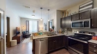 This single-floor, 2-bedroom, 2-bathroom unit offers a thoughtfully designed open-concept layout that connects the kitchen and living area seamlessly. The kitchen is a functional centerpiece, featuring dark espresso cabinetry, granite countertops, a peninsula with a double sink, and a full suite of stainless steel appliances including a refrigerator, range, microwave, and dishwasher. Pendant lighting over the peninsula adds a modern touch, while wood-look flooring grounds the space with warmth and durability.

The living area flows naturally from the kitchen, benefiting from natural light through windows dressed with blinds and curtain panels. Both bedrooms are carpeted and feature ceiling fans, neutral walls, and windows that allow ample natural light. Each room offers a comfortable, private retreat with good proportions for furnishing.

The two bathrooms mirror each other in design, each featuring large-format light tile flooring, a full tub-shower combination, and a clean, neutral aesthetic. The overall design palette throughout the unit is consistent—neutral tones, dark accents, and modern fixtures—creating a cohesive and functional living environment.