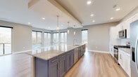 Located at 6842 Main St in Buffalo, NY, this well-appointed 1-bedroom, 1-bathroom residence offers a thoughtfully designed open-concept layout across a single floor. The combined kitchen and living area serves as the heart of the home, showcasing a striking oversized island with polished granite countertops, dual-tone cabinetry featuring navy lower cabinets and crisp white uppers with brushed gold hardware, and stainless steel appliances. Elegant pendant lighting hangs above the island, complementing the recessed lighting throughout. Large floor-to-ceiling windows flood the living area with abundant natural light and frame sweeping outdoor views of the surrounding neighborhood. Light-toned hardwood-style flooring flows seamlessly through the main living spaces, adding warmth and continuity. The bedroom is a comfortable retreat, finished with plush carpeting, a ceiling fan, and a sliding glass door opening to a private balcony with outdoor views. A second window further brightens the space. The bathroom features a double-sink granite vanity with white cabinetry and modern brushed nickel fixtures, offering both style and functionality. The overall ambiance is clean, contemporary, and move-in ready.