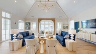 Located at 7785 Griffon Ln in Vero Beach, Florida, this single-floor amenity space offers a generously proportioned layout designed to blend coastal elegance with functional versatility. The centerpiece is a breathtaking great room crowned by a soaring vaulted shiplap ceiling, anchored by a gold sputnik chandelier and a striking reclaimed wood archway that frames large French doors opening to outdoor views. Navy blue sofas, striped accent chairs, and natural fiber rugs create a refined yet relaxed coastal atmosphere throughout. Light oak hardwood flooring runs seamlessly through the space, enhancing its airy, sun-filled character. Multiple dining rooms provide flexible gathering spaces, each thoughtfully appointed — one features a woven rattan pendant light above a long conference table with leather chairs, while another doubles as a combined dining and kitchen area. The kitchen is outfitted with white cabinetry, quartz countertops, gold hardware, a stainless steel sink, and eye-catching blue mosaic tile backsplash, all bathed in natural light from oversized windows. Office spaces include a dedicated conference room and cozy built-in desk nooks enclosed by glass-paned French doors. The entrance areas are welcoming and tastefully decorated, setting a polished coastal tone from the moment of arrival.