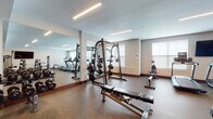 The fitness center at 40 Bennett Rd in Englewood, New Jersey, is a thoughtfully designed, single-floor facility offering a comprehensive range of exercise spaces and equipment. The layout is divided into distinct functional zones, each tailored to specific training needs.

The main strength training area features durable rubber flooring and is lined with large floor-to-ceiling mirrors that enhance the sense of space and allow users to monitor their form. This zone is well-stocked with a full rack of dumbbells in varying weights, a multi-function Smith machine, an adjustable weight bench, and additional free weight equipment. Linear LED lighting installed across the ceiling provides consistent, even illumination throughout.

An adjacent cardio area houses multiple treadmills and upright cardio machines positioned near windows that allow natural light to filter in. Wall-mounted flat-screen televisions are positioned for comfortable viewing during workouts.

A separate functional training studio features wood-look flooring, a wall-mounted TV, large mirrors, TRX suspension trainers, medicine balls, plyo boxes, and a dedicated equipment rack—ideal for group or circuit-style training. The studio benefits from recessed and pendant lighting, adding a polished aesthetic.

The facility is accessed through teal-framed glass double doors and includes a cable machine station and additional strength equipment near the entrance. The overall ambiance is clean, modern, and well-maintained.