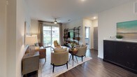 The B3 floor plan is a thoughtfully designed two-bedroom, two-bathroom residence that combines modern aesthetics with functional living spaces across a single floor. Rich wood-style flooring flows throughout the main living areas, anchoring the open-concept layout.

The kitchen is a standout feature, showcasing two-tone cabinetry with white upper cabinets and wood-finish lower cabinets, granite countertops, a grey tile backsplash, stainless steel appliances, and a tray ceiling with accent lighting. Ample storage is provided through a full-height pantry cabinet and open shelving.

The living room is bright and welcoming, with large sliding glass doors that open to a private balcony with outdoor views, complemented by a ceiling fan and recessed lighting. The dining area connects seamlessly to both the kitchen and living room.

Each bedroom offers plush carpeting, ceiling fans, and generous natural light from large windows. The primary bedroom includes an en-suite bathroom featuring a granite-topped vanity, wood-finish cabinetry, dark hardwood-style flooring, and a glass-enclosed shower. A spacious walk-in closet with multi-level shelving and hanging rods provides extensive storage. The second bathroom features a dual-sink vanity with granite countertops and a soaking tub with tiled surround.