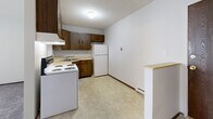 Located at 330 29th Street Dr SE in Cedar Rapids, Iowa, this one-bedroom, one-bathroom unit offers a practical and efficient single-floor layout. The kitchen is equipped with dark wood cabinetry spanning both upper and lower sections, a white electric range, a full-size refrigerator, and a single-basin sink with light countertops. Vinyl tile flooring runs throughout the kitchen, providing easy maintenance. A small breakfast bar divides the kitchen from the adjacent living area, which features neutral carpet and a window with vertical blinds that allows natural light to filter in. The bedroom is a comfortable, carpeted space highlighted by a ceiling fan with integrated lighting, a window with vertical blinds, and a baseboard heating unit. Two closets provide ample storage throughout the unit. The bathroom includes a full-size soaking tub with a tiled surround in a classic neutral palette, complemented by a chrome towel bar and vinyl tile flooring. Throughout the unit, white walls and dark wood baseboards create a clean, consistent aesthetic. Baseboard heating is present in multiple rooms, ensuring warmth during Iowa's cold months.