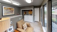 Located at 3801 N Belt Line Rd in Irving, Texas, this single-story community laundry facility combines practical functionality with a welcoming ambiance. The space is thoughtfully designed with warm, neutral gray walls and light wood-style flooring that lend a clean, contemporary feel throughout.

The laundry area is well-equipped with multiple top-load washing machines and dryers, including a dedicated alcove housing a washer and dryer set accented by decorative gold sunburst wall art, adding a stylish touch to an otherwise utilitarian space. Additional coin-operated machines are positioned along the walls, providing ample capacity for residents.

A comfortable seating nook is incorporated into the layout, furnished with a plush tan armchair and a coordinating accent chair, a wooden side table, and decorative accessories — offering a relaxed waiting area. A tall decorative plant adds a natural, lively element to the corner.

Large windows along one wall flood the space with natural light and provide views of the outdoor grounds, including a fenced recreational area with greenery, creating an open and airy atmosphere. Flush-mount circular ceiling lights ensure bright, even illumination throughout. A fire extinguisher is visibly mounted for safety, and a door provides convenient exterior access to the surrounding property.