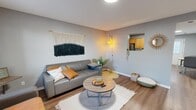 Located at 1095 Spruce St in Terre Haute, Indiana, this 2-bedroom, 1-bathroom apartment offers a thoughtfully arranged single-floor layout that maximizes every square foot. The living room serves as the heart of the home, featuring warm wood-look flooring, neutral gray walls, and an eye-catching macramé wall hanging that adds a distinct bohemian character. A pass-through window connects the living area to the kitchen, enhancing the open feel between spaces. The kitchen is well-equipped with warm wood cabinetry, granite-style countertops, stainless steel appliances including a refrigerator and dishwasher, and a black range. Recessed lighting and a windowed door brighten the space, which also accommodates a dining area. Both bedrooms offer natural light through multiple windows dressed with soft, sheer curtains. The primary bedroom provides a comfortable, well-proportioned retreat with hardwood-style flooring and ample room for a desk workspace. The shared bathroom features a wood-toned vanity, white countertop, and a large mirror. A connecting hallway ties all rooms together seamlessly. Throughout the apartment, consistent flooring and a cohesive cool-gray palette create a unified, modern aesthetic.