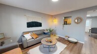 Located at 1095 Spruce St in Terre Haute, Indiana, this 2-bedroom, 1-bathroom apartment offers a thoughtfully arranged single-floor layout that maximizes every square foot. The living room serves as the heart of the home, featuring warm wood-look flooring, neutral gray walls, and an eye-catching macramé wall hanging that adds a distinct bohemian character. A pass-through window connects the living area to the kitchen, enhancing the open feel between spaces. The kitchen is well-equipped with warm wood cabinetry, granite-style countertops, stainless steel appliances including a refrigerator and dishwasher, and a black range. Recessed lighting and a windowed door brighten the space, which also accommodates a dining area. Both bedrooms offer natural light through multiple windows dressed with soft, sheer curtains. The primary bedroom provides a comfortable, well-proportioned retreat with hardwood-style flooring and ample room for a desk workspace. The shared bathroom features a wood-toned vanity, white countertop, and a large mirror. A connecting hallway ties all rooms together seamlessly. Throughout the apartment, consistent flooring and a cohesive cool-gray palette create a unified, modern aesthetic.