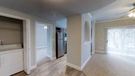 This two-bedroom, two-bathroom single-floor residence offers a thoughtfully arranged layout that maximizes functionality and comfort. The interior features a neutral color palette with warm greige walls and crisp white trim, creating a clean, cohesive aesthetic throughout. Wood-style hard flooring runs through the main living and kitchen areas, while plush carpeting adds warmth to the bedrooms and additional living spaces.

The kitchen is equipped with stainless steel appliances, including a full-size refrigerator and microwave, complemented by dark cabinetry that provides a stylish contrast to the lighter surroundings. A distinctive arched architectural detail adds character to the space, serving as a decorative dividing element between areas. Crown molding accents enhance the overall finish of the unit.

The bedrooms are carpeted and generously proportioned, with one featuring a ceiling fan for added comfort. The open flow between the main corridor, kitchen, and living areas contributes to an airy, connected feel. Overall, the space balances practical design with tasteful architectural details, making it a comfortable and visually appealing residence.