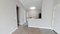 This single-floor, one-bedroom, one-bathroom unit offers a practical and well-organized layout designed to maximize the available living space. The open-concept design connects the living area to the kitchen, creating a seamless flow throughout the main living zone.

The kitchen is defined by a peninsula-style breakfast bar with dark countertops, providing both workspace and a casual dining option. A black refrigerator anchors the kitchen, which also features hard-surface flooring for easy maintenance. The neutral gray-toned walls create a clean, modern aesthetic throughout the unit.

The living area is finished with plush carpet, offering a comfortable contrast to the hard flooring in the kitchen and entry areas. Flush-mount ceiling lighting provides consistent illumination across the space. Visible HVAC vents indicate a central climate control system throughout.

A hallway visible from the main living area leads to the bedroom and bathroom, ensuring a well-defined separation between the private and shared spaces. White panel doors and crisp white trim contribute to the unit's clean, contemporary finish. The overall ambiance is bright, neutral, and move-in ready.