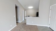 This single-floor, one-bedroom, one-bathroom unit offers a practical and well-organized layout designed to maximize the available living space. The open-concept design connects the living area to the kitchen, creating a seamless flow throughout the main living zone.

The kitchen is defined by a peninsula-style breakfast bar with dark countertops, providing both workspace and a casual dining option. A black refrigerator anchors the kitchen, which also features hard-surface flooring for easy maintenance. The neutral gray-toned walls create a clean, modern aesthetic throughout the unit.

The living area is finished with plush carpet, offering a comfortable contrast to the hard flooring in the kitchen and entry areas. Flush-mount ceiling lighting provides consistent illumination across the space. Visible HVAC vents indicate a central climate control system throughout.

A hallway visible from the main living area leads to the bedroom and bathroom, ensuring a well-defined separation between the private and shared spaces. White panel doors and crisp white trim contribute to the unit's clean, contemporary finish. The overall ambiance is bright, neutral, and move-in ready.