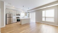 This single-floor unit offers a well-designed layout across two bedrooms and three bathrooms, making efficient use of its compact footprint. The open-concept kitchen and living area serves as the heart of the space, featuring light hardwood flooring, a tray ceiling with recessed lighting, and two sleek pendant lights that anchor the central kitchen island. White shaker-style cabinetry lines the kitchen walls, complemented by a white subway tile backsplash, light quartz countertops, and a full suite of stainless steel appliances including a refrigerator, range, and over-the-range microwave. A sliding glass door with vertical blinds brings in natural light and connects the living area to the exterior. The bedrooms feature neutral-toned carpet and windows fitted with roller shades, providing a calm and restful atmosphere. The primary bedroom is a comfortable size with its own dedicated bathroom. The bathrooms are finished consistently throughout, with white vanities featuring black hardware accents, light hardwood-style flooring, and glass-enclosed walk-in showers. A hallway and closet complete the layout, adding practical storage to the unit's overall functionality.