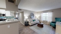 This single-floor residence offers a thoughtfully designed layout with a cohesive neutral color palette and wood-style flooring that runs through the main living areas. The living room serves as the heart of the unit, featuring a textured ceiling, natural light from windows dressed with sheer curtains and blinds, and an open sightline to the kitchen via a pass-through counter. The kitchen is well-equipped with stainless steel appliances, including a refrigerator, range, and microwave, complemented by white cabinetry, light countertops, and a teal subway tile backsplash that adds a subtle coastal accent.

The unit includes multiple bedrooms, each finished with plush carpet and ample closet access. One bedroom features a tufted upholstered headboard with teal accents, while another is styled with a classic white headboard and navy striped bedding. The bathroom includes a tub-shower combination with white tile surround, a single-sink vanity with white cabinetry, and wood-style flooring. A dedicated laundry area with shelving above the washer provides additional storage and practical convenience within the unit.