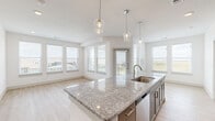 This well-appointed 2-bedroom, 2-bathroom single-floor residence offers a thoughtfully designed open-concept layout that maximizes both functionality and comfort. The combined kitchen and living area serves as the heart of the home, featuring a large granite island with a dual-basin sink, elegant pendant lighting, and rich taupe cabinetry paired with a full suite of stainless steel appliances including a refrigerator, electric range, and microwave. Light wood-style flooring flows throughout the main living areas, complemented by crisp white walls that enhance the bright, airy atmosphere. Expansive windows in the living area frame outdoor views and flood the space with natural light. A central hallway connects the bedrooms and bathrooms, maintaining a clean and organized flow. Both bedrooms are carpeted for comfort and include ceiling fans; the primary bedroom features an en-suite bathroom with a dual-sink granite vanity and tiled tub-shower combination. The secondary bathroom mirrors the same quality finishes. Three closets provide generous storage throughout. The space also includes a private exterior access point, rounding out this modern and move-in-ready residence.
