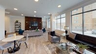 Located at 2150 Bond St. in Charlottesville, Virginia, this single-floor amenity space combines contemporary design with inviting functionality. The entrance features wood-look tile flooring, crown molding, and a striking sputnik chandelier, with sleek black-framed glass partition doors lending a modern, upscale character to the welcome area.

The open-concept clubroom serves as the heart of the space, anchored by a dramatic dark stacked-stone accent wall that contrasts beautifully against white walls and light flooring. A large flat-screen TV and comfortable seating arrangements create an ideal lounge setting, while decorative pendant lights and recessed ceiling lights maintain a warm, sophisticated ambiance throughout.

The kitchen area features a generous granite-topped island with bar seating, stainless steel appliances, and globe pendant lighting suspended above—perfect for social gatherings. The dark stone backsplash ties cohesively into the room's overall design aesthetic.

A sun-filled lounge extends the space further, boasting an abundance of large windows that flood the room with natural light and offer views of the surrounding neighborhood. Columns with crown molding detailing add architectural interest to this airy retreat.

The fitness center is well-appointed with Matrix cardio equipment, wall-mounted televisions, rubberized flooring, and a ceiling fan, providing a clean and functional workout environment for residents.
