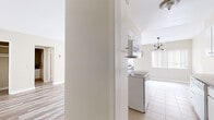 Located on N Doheny Drive in Beverly Hills, this single-story unit offers a clean, neutral palette throughout, with light-toned walls and consistent light wood laminate flooring connecting the main living areas. The open living and dining area is generously proportioned, allowing for flexible furniture arrangements. A sliding glass door draws in natural light and provides access to an outdoor area, while a contemporary chandelier adds a subtle design accent overhead.

The galley-style kitchen is efficiently laid out, featuring white cabinetry, dark granite countertops, a white double sink, matching white appliances including an electric range, and a built-in microwave. Tile flooring runs through the kitchen, which also benefits from access to an adjoining storage or utility area.

The bedrooms continue the light wood flooring theme and receive natural light through standard windows. One bedroom features a mirrored sliding-door closet with gold-toned hardware, providing ample storage. The bathroom is equipped with a granite vanity countertop, an integrated sink, a full-length mirror, and a separate shower enclosure with tile flooring. The overall ambiance of the unit is clean, bright, and move-in ready, reflecting the desirable Beverly Hills location.