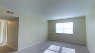 This single-floor space presents a clean, straightforward layout designed for comfortable everyday living. The main room is generously proportioned, offering an open and airy feel that provides flexibility for a variety of furnishing arrangements. Neutral, light yellow-beige walls create a calm and welcoming atmosphere, complementing the soft grey carpeted flooring that runs throughout the space. A centrally positioned window allows natural light to pour in, casting bright patches across the floor and enhancing the overall sense of openness. The textured white ceiling adds a subtle visual element while keeping the room feeling bright and spacious. White baseboards run along the perimeter, providing clean, crisp contrast against the walls and carpet. Electrical outlets are conveniently positioned along the walls, offering practical functionality. The overall ambiance of the space is neutral and move-in ready, making it an ideal canvas for personalization. The simplicity of the design ensures that the space can adapt to a wide range of uses, from a living area to a bedroom or multipurpose room. The abundance of natural light and the understated color palette together create an inviting and versatile environment.