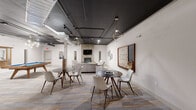 Located at 1 E Main St in Bay Shore, NY, this generously sized single-floor amenity space offers a well-rounded mix of recreation, fitness, and social areas designed for modern communal living. The welcoming hallway sets the tone with warm pendant lighting, multi-toned patterned carpeting, and a clean, neutral color palette accented by a sleek marble-top accent table.

The open lounge area serves as the social centerpiece, featuring exposed dark ceilings with industrial-style ductwork, a striking brick accent wall, a fireplace, and a wall-mounted TV. Comfortable seating arrangements with plush sofas in gray and gold tones invite relaxation, while a full-size pool table adds a recreational focal point. Statement lighting fixtures, including geometric and cluster pendants, lend an upscale urban character throughout.

The dining room stands out with its dramatically dark ceiling contrasting white walls, draped Edison bulb pendant lighting, and a textured feature wall. Sturdy wood dining tables paired with contemporary white chairs create a stylish, functional gathering space.

The fitness center is equipped with cardio machines including treadmills, a stationary bike, and a cycling bike, complemented by rubberized flooring, wall-to-wall mirrors, exposed ceiling infrastructure, and ceiling fans for ventilation. An additional open flexible room with hardwood-style flooring and wall sconce lighting offers versatile use potential.