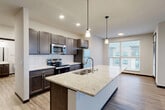 Located at 3401 E Washington Ave in Madison, WI, this well-appointed 3-bedroom, 2-bathroom single-floor residence offers a thoughtfully designed layout with modern finishes throughout. The open-concept kitchen and living area serves as the heart of the home, featuring a large granite-topped island with pendant lighting, dark espresso cabinetry, a white subway tile backsplash, and a full suite of stainless steel appliances. Wood-plank flooring flows through the main living space, which is brightened by expansive windows offering outdoor views. The primary bedroom is a comfortable, carpeted retreat with a built-in closet and direct access to a private bathroom equipped with a vanity featuring granite countertops and wood cabinetry. Two additional bedrooms offer carpeted or wood-floor finishes, providing versatile spaces for various needs. A second full bathroom includes a tub-shower combination with clean white surroundings. Dark-framed interior doors with frosted glass panels lend a contemporary aesthetic throughout the hallways and entry. The unit also includes a dedicated laundry area and multiple closets for ample storage. The overall design balances modern style with functional living.