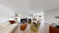 This single-floor, 2-bedroom, 1-bathroom residence offers a thoughtfully designed layout across a comfortable footprint. The open-plan living and dining area serves as the heart of the home, anchored by a striking dark-tiled fireplace and sliding glass doors that lead to a private outdoor patio, allowing natural light to pour in and providing pleasant outdoor views. Light hardwood-style flooring flows throughout the main living areas, complementing the clean white walls and creating a bright, cohesive aesthetic.

The galley kitchen is efficiently arranged with white shaker cabinetry, gray tile backsplash, dark countertops, a stainless steel sink, and stainless steel appliances, including a refrigerator and gas range. The dining area, positioned adjacent to the living room, benefits from large windows dressed with linen curtains that frame natural light beautifully.

The primary bedroom offers a comfortable, carpeted retreat, while the second bedroom features built-in shelving and a dedicated closet nook, also with soft carpet flooring. The full bathroom includes a tiled shower-tub combination. Two hallways and a dedicated closet contribute to the home's practical storage and circulation. The entrance area provides a welcoming transition into the living space, completing this well-organized and inviting residence.