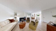 This single-floor, 2-bedroom, 1-bathroom residence offers a thoughtfully designed layout across a comfortable footprint. The open-plan living and dining area serves as the heart of the home, anchored by a striking dark-tiled fireplace and sliding glass doors that lead to a private outdoor patio, allowing natural light to pour in and providing pleasant outdoor views. Light hardwood-style flooring flows throughout the main living areas, complementing the clean white walls and creating a bright, cohesive aesthetic.

The galley kitchen is efficiently arranged with white shaker cabinetry, gray tile backsplash, dark countertops, a stainless steel sink, and stainless steel appliances, including a refrigerator and gas range. The dining area, positioned adjacent to the living room, benefits from large windows dressed with linen curtains that frame natural light beautifully.

The primary bedroom offers a comfortable, carpeted retreat, while the second bedroom features built-in shelving and a dedicated closet nook, also with soft carpet flooring. The full bathroom includes a tiled shower-tub combination. Two hallways and a dedicated closet contribute to the home's practical storage and circulation. The entrance area provides a welcoming transition into the living space, completing this well-organized and inviting residence.