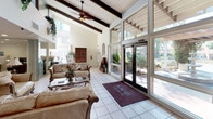 This residential community showcases a cohesive Spanish-inspired architectural style, characterized by warm earth-toned stucco exteriors and distinctive red clay tile rooflines that lend a classic Mediterranean character to the buildings. The community entrance is marked by an elegant multi-tiered stone fountain, flanked by towering palm trees and carefully maintained shrubbery, creating an inviting first impression. A leasing office with large glass-front entry doors and a low-profile roofline serves as the central hub of the property.

The grounds are a standout feature of this community, with expansive, well-manicured lawns stretching between buildings. Curved concrete walkways wind through the green spaces, connecting residents to individual buildings while passing beneath the shade of mature trees. Neatly trimmed hedgerows and decorative plantings line the building perimeters, adding structure and visual appeal to the landscape.

The multi-building layout provides a sense of openness and breathing room between structures, while exterior staircases and private balconies offer residents individual outdoor access. The overall ambiance is calm, park-like, and well-maintained, reflecting a community designed with outdoor livability and curb appeal in mind.
