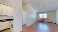 This single-floor 1-bedroom, 1-bathroom residence offers a clean and functional layout designed for comfortable everyday living. The living area is a welcoming space highlighted by warm hardwood flooring that runs throughout, creating a cohesive and inviting atmosphere. A large window allows natural light to pour in, brightening the room and enhancing its open feel. A distinctive vertically paneled white accent wall adds a subtle architectural detail, providing visual interest and a touch of character to the space. A wall-mounted HVAC unit and baseboard heating ensure year-round climate comfort. The layout connects seamlessly to additional areas of the unit, with a hallway leading to the private bedroom and bathroom. The kitchen is positioned conveniently off the main living space, offering easy accessibility. The overall color palette is neutral and light, with white walls and soft tones that create a calm, airy ambiance throughout. The unit's straightforward, single-level design makes it easy to navigate, while the combination of practical features and natural light makes it a comfortable and functional home.