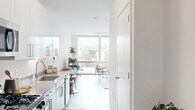 This thoughtfully designed single-floor unit offers a clean, modern aesthetic throughout, characterized by a crisp white color palette, light wood-style flooring, and an open-concept layout that maximizes every inch of the space. Large floor-to-ceiling windows in the living room flood the interior with natural light and provide views of the surrounding neighborhood, creating an airy, welcoming atmosphere.

The kitchen is efficiently designed with white upper cabinetry, sleek gray lower cabinets, granite countertops, and a full suite of stainless steel appliances including a gas range, over-the-range microwave, refrigerator, and dishwasher. A small dining area adjacent to the kitchen accommodates a compact table, making it a functional space for everyday meals.

The living room is bright and open, anchored by the expansive windows and offering ample room for seating and relaxation. The neutral tones and clean lines throughout lend a contemporary, cohesive feel to the shared living area.

The bathroom is well-appointed with a full tub and shower combo, large-format tile surround in warm gray tones, a granite-topped vanity, and brushed nickel fixtures, providing a polished, functional finish. Overall, the space presents a modern and efficiently organized layout suited for comfortable everyday living.