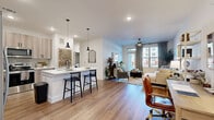 Located in Katy, TX, this thoughtfully designed one-bedroom, two-bathroom residence offers a seamless open-concept floor plan with warm wood-look flooring and crisp white walls throughout. The kitchen is a standout feature, equipped with stainless steel appliances including a French door refrigerator, built-in wine cooler, and a range with microwave. Light wood cabinetry extends to the ceiling for ample storage, while a white quartz island with bar seating and a tile backsplash complete the contemporary aesthetic. The kitchen flows directly into a bright, airy living room anchored by large windows with floor-to-ceiling drapes, a ceiling fan, and access to an outdoor area. The spacious primary bedroom accommodates a king-sized bed comfortably, features generous natural light through large windows, and connects to a well-designed en-suite bathroom with dual sinks, wood-toned cabinetry, black fixtures, and a deep soaking tub surrounded by neutral stone-look tile. A dedicated closet and a second full bathroom add everyday practicality. The overall ambiance is modern and inviting, with consistent finishes creating a cohesive and polished living environment.