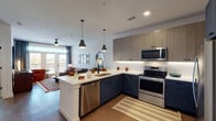 Located at 2439 Beatrice St in Dallas, Texas, this single-floor residence offers a thoughtfully designed layout with contemporary finishes throughout. The open-concept kitchen is a standout feature, showcasing two-tone cabinetry with navy lower cabinets and light wood upper cabinets, white subway tile backsplash, quartz countertops, and a full suite of stainless steel appliances. A peninsula island with seating for multiple guests and pendant lighting creates a natural gathering space that flows seamlessly into the dining and living areas. The living room is bright and inviting, featuring large French doors that open to a private balcony with outdoor views, allowing generous natural light to fill the space. The bedroom continues the modern aesthetic with large windows dressed in layered curtains and blinds, providing both natural light and privacy, along with light wood-style flooring found throughout the unit. The primary bathroom is well-appointed with dual sinks set in navy cabinetry, a walk-in glass-enclosed shower with white tile surround, and direct access to a walk-in closet with built-in shelving. A stacked in-unit washer and dryer is conveniently located within the bathroom. Clean white walls, recessed lighting, and a cohesive neutral palette with warm accent tones give the entire residence a polished and modern feel.