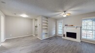This single-floor residence offers a cohesive, neutral aesthetic throughout, highlighted by durable hardwood-style flooring that flows seamlessly from room to room. The living area serves as the heart of the space, centered around a classic white brick fireplace with a traditional mantle. A built-in shelving unit flanks one wall, providing practical display and storage space, while a ceiling fan overhead ensures year-round comfort. Natural light filters in through a window with shutters, brightening the open layout. The living area connects directly to a galley-style kitchen, which is efficiently designed with gray cabinetry, granite-patterned countertops, a double stainless steel sink, a dishwasher, and a stainless steel range. A window at the end of the kitchen brings in additional natural light. The bedroom is a well-proportioned, tranquil space featuring its own ceiling fan, hardwood-style flooring, and a generously sized window dressed with blinds. The bathroom is clean and functional, appointed with a gray vanity, granite-style countertop, a medicine cabinet mirror, and a full tub and shower combination. A textured ceiling is consistent throughout the space, adding a subtle classic character to the overall design.