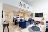 Located at 2502 Packard St in Ann Arbor, MI, this two-story residence offers a thoughtfully designed layout spread across two well-proportioned floors. The main level immediately impresses with dramatic double-height ceilings in the open-concept living and kitchen area, flooding the space with an airy, loft-like atmosphere. Floor-to-ceiling windows with roller shades draw in natural light, enhancing the clean, contemporary aesthetic throughout.

The kitchen is outfitted with stainless steel appliances, including a refrigerator, range, and microwave, complemented by light wood upper cabinetry, dark lower cabinets, and a white quartz countertop island with bar seating — ideal for casual dining or entertaining. The living area flows seamlessly from the kitchen and features neutral-toned flooring and a staircase leading to the upper level.

Upstairs, the generously sized primary bedroom offers light wood flooring, recessed lighting, and an open layout with ample room for furnishings. A dedicated closet provides convenient storage. The residence includes two well-appointed bathrooms, one of which features striking geometric-patterned tile flooring, adding a stylish design touch. An in-unit laundry area with a full-size washer and dryer completes the home's practical amenities, making this a well-rounded and functional living space.