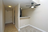 This single-floor unit is designed with a practical, open layout that maximizes functionality across its living spaces. The living area is a standout feature, boasting notably elevated ceilings with high clerestory windows that allow natural light to filter in from above, creating a bright and airy atmosphere. A ceiling fan is centrally positioned, enhancing airflow throughout the space. Neutral-toned carpet covers the living and bedroom areas, contributing to a cohesive and understated aesthetic.

The kitchen is efficiently arranged with a peninsula-style breakfast bar that opens toward the living area, promoting an inclusive feel. Built-in appliances are integrated into the cabinetry, and the entryway connects directly to this functional cooking space via wood-look flooring.

The bedroom is generously proportioned, featuring plush carpet, a ceiling fan, and a large sliding glass door dressed with full-length vertical blinds that provide both privacy and light control. A double-door closet offers ample storage.

The bathroom includes a sleek, elongated white vanity countertop with an undermount sink, dark wood cabinetry below, brushed nickel fixtures, and dual wall-mounted mirrors above, providing a clean and modern finish throughout.