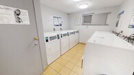 Located at 7-11 Rochefort Dr in Toronto, Ontario, this shared laundry facility offers a practical and well-equipped space for residents. The room features light grey walls and durable yellow tile flooring throughout, creating a clean and functional environment. Multiple front-loading Huebsch washers and dryers by Coinamatic are arranged along the walls, providing ample capacity for resident use. The machines support both card and mobile app-based payments via the Coinamatic smart laundry portal, offering convenient and modern payment options. Ventilation is provided through a louvered wall vent, ensuring adequate airflow within the space. A fire extinguisher is mounted on the wall, and informational postings—including laundry tips, usage instructions, and safety notices—are displayed prominently throughout the room. Flush-mount ceiling lighting provides even illumination across the space. Access is through a solid grey door with a secure latch. The layout is straightforward and efficiently organized, maximizing the usable floor area for equipment and user access. Overall, the facility is well-maintained and designed to meet the day-to-day laundry needs of the building's residents in a no-frills, functional setting.