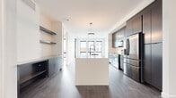 Located on Dell Cort Drive in Brecksville, Ohio, this contemporary single-floor residence showcases a thoughtfully designed open-concept layout with high-end finishes throughout. The kitchen serves as the centerpiece of the space, featuring dark cabinetry paired with a striking white quartz island, stainless steel appliances, a deep basin sink with a professional-style faucet, open floating shelves, and a statement oval pendant light that anchors the room. Rich, dark hardwood flooring runs throughout the kitchen and living areas, contrasting beautifully with the bright white walls and ceilings.

The living area benefits from an abundance of natural light, courtesy of a wall of large black-framed floor-to-ceiling windows and a sliding glass door that opens to a private balcony with sweeping views of the surrounding Brecksville community. Additional rooms feature the same light-toned hardwood flooring, crisp white walls, and generous window coverage that frames outdoor scenery.

The bathroom is finished to a high standard, with a gray floating vanity, backlit mirror, quartz countertop, large-format porcelain tile flooring, and a glass-enclosed walk-in shower with white tile surround and matte black fixtures. A dedicated hallway utility area includes a stacked washer and dryer alongside built-in open shelving for convenient storage, completing this well-appointed modern residence.
