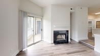 Located at 150 Commons Way in Doylestown, PA, this one-bedroom, one-bathroom residence offers a well-designed layout with modern finishes and a warm, inviting ambiance. The open-concept living and kitchen area is anchored by a striking black-tiled fireplace with a white mantel, complemented by hardwood-style flooring and neutral walls that maximize the natural light streaming in through multiple windows. A sliding glass door leads directly to a private outdoor deck, creating a seamless indoor-outdoor connection. The kitchen is appointed with two-tone cabinetry—sleek white upper cabinets and wood-toned lower cabinets—paired with white countertops, a blue tile backsplash, and a full suite of stainless steel appliances. The bedroom features plush carpeting, generous natural light from large windows with views of lush greenery, and access to a dedicated closet. The bathroom is thoughtfully finished with wood-look floor tile, a matching tiled tub surround, a soaking tub, and a modern vanity with ample counter space. A dedicated in-unit laundry area with a full-size washer and dryer adds everyday convenience. The overall aesthetic is clean, contemporary, and move-in ready.
