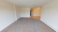Located at 8301 S Cork Ave in Justice, IL, this single-floor unit offers a practical and comfortable layout across several well-defined rooms. The spacious living area is finished with neutral-toned carpet and features a sliding glass door that opens to a balcony, allowing natural light to fill the space and offering outdoor views. Baseboard heating runs along the walls throughout the unit, providing efficient climate control. An additional carpeted room with a window overlooking greenery serves well as a bedroom or flexible living space, also equipped with baseboard heating and a wall-mounted AC unit. The kitchen is outfitted with ample cabinetry in a warm brown finish, a gas range, a full-size refrigerator, a double-basin sink, and a tile backsplash, offering a fully functional cooking environment with tile flooring. The full bathroom features tile flooring, a wood-toned vanity with a medicine cabinet mirror, and a tiled tub-surround shower with a decorative border accent and chrome fixtures. Additional bedrooms are carpeted and bright, with windows framing natural views. The unit's clean, neutral palette throughout creates a move-in ready environment suitable for a variety of lifestyles.