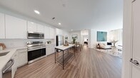 Located at Modera 2 in Pine Brook, NJ, this well-appointed 2-bedroom, 2-bathroom residence offers a thoughtfully designed single-floor layout that maximizes functionality and modern style. Wood-look flooring flows seamlessly throughout the main living areas, anchoring a cohesive and contemporary aesthetic.

The open-concept kitchen, dining, and living area forms the heart of the home. The kitchen is outfitted with high-gloss white cabinetry reaching toward the ceiling, a light-toned tile backsplash, stainless steel appliances including a refrigerator, range, microwave, and dishwasher, and a marble-topped island that doubles as a prep and gathering space. The adjoining dining area accommodates a glass-top table, while the living room offers generous natural light through large windows dressed in sheer curtains, complemented by crisp white walls ideal for artwork display.

The spacious primary bedroom features a closet and neutral carpeting, creating a calm retreat. The second bedroom is equally well-proportioned with its own closet. Both bathrooms are finished with wood-look tile flooring, modern vanities with backlit mirrors, and clean white surrounds. The overall ambiance is bright, clean, and move-in ready.