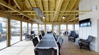 Located at 1015 Nutt Street in Wilmington, NC, this single-story waterfront space offers a captivating blend of rustic craftsmanship and open-air design along the Cape Fear River. The structure is defined by its impressive exposed wood timber framing and beam ceiling, which lend a warm, pavilion-like character to the interior. Large open-air openings line the perimeter, flooding the space with natural light and providing panoramic views of the surrounding marina and waterway. A generous communal dining table, flanked by wicker lounge chairs, serves as the centerpiece of the main gathering area, making it well-suited for group events or casual waterfront dining. Pendant lighting hangs in clusters from the timber ceiling, adding an industrial yet inviting touch to the atmosphere. The light-toned wood plank flooring complements the natural palette of the structure throughout. Additional seating areas near the open edges of the space allow guests to take full advantage of the outdoor scenery. The overall ambiance is relaxed and airy, with the sounds and sights of the waterfront seamlessly integrated into the experience, making this a distinctive and memorable destination on the Wilmington riverfront.