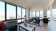 This two-bedroom, two-bathroom residence is defined by its striking corner placement, featuring expansive floor-to-ceiling windows that wrap around the living and dining areas to frame panoramic city skyline views. Natural light floods the open-plan living space throughout the day, creating a bright and airy atmosphere that enhances the clean, modern aesthetic.

The living area is generously proportioned, accommodating a comfortable seating arrangement centered around a rectangular coffee table atop a textured area rug. Warm leather accent chairs complement the neutral palette of white walls and light hardwood flooring, striking a balance between contemporary style and approachable comfort.

Adjacent to the living space, the dining area takes full advantage of the corner window configuration, with teal upholstered chairs gathered around a round table—an intimate setting with a dramatic urban backdrop. The seamless flow between the living and dining zones makes the space well-suited for both everyday living and entertaining.

The residence spans a single floor, offering a cohesive and easily navigable layout. The elevated position of the unit provides unobstructed sightlines across the city, making the sweeping skyline views a defining and standout feature of the home.