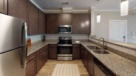 Located at 503 Carowill Dr in Greensboro, NC, this single-floor residence offers a well-designed, open-concept layout with a cohesive blend of modern finishes throughout. The kitchen serves as the focal point of the living space, featuring rich dark cabinetry, granite countertops with speckled detailing, a subway tile backsplash, and a full suite of stainless steel appliances including a refrigerator, electric range, microwave, and dishwasher. A peninsula with an integrated double sink and pendant lighting overhead connects the kitchen seamlessly to the living area, which is finished with wood-style plank flooring, crown molding, and a ceiling fan. Natural light enters through slatted blinds on multiple windows, and direct exterior access is available via a secondary door. The bedroom features plush carpeting, a ceiling fan, and opens to a walk-in closet with built-in shelving. The bathroom is appointed with granite countertops, dark cabinetry, a large mirror, and a tub-shower combination. A second bathroom offers a similar layout with generous floor space and wood-style flooring. Crown molding and neutral warm-toned walls carry throughout, lending the space a clean and cohesive aesthetic.