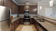 Located at 503 Carowill Dr in Greensboro, NC, this single-floor residence offers a well-designed, open-concept layout with a cohesive blend of modern finishes throughout. The kitchen serves as the focal point of the living space, featuring rich dark cabinetry, granite countertops with speckled detailing, a subway tile backsplash, and a full suite of stainless steel appliances including a refrigerator, electric range, microwave, and dishwasher. A peninsula with an integrated double sink and pendant lighting overhead connects the kitchen seamlessly to the living area, which is finished with wood-style plank flooring, crown molding, and a ceiling fan. Natural light enters through slatted blinds on multiple windows, and direct exterior access is available via a secondary door. The bedroom features plush carpeting, a ceiling fan, and opens to a walk-in closet with built-in shelving. The bathroom is appointed with granite countertops, dark cabinetry, a large mirror, and a tub-shower combination. A second bathroom offers a similar layout with generous floor space and wood-style flooring. Crown molding and neutral warm-toned walls carry throughout, lending the space a clean and cohesive aesthetic.