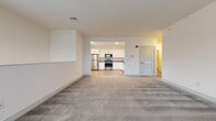 Located at 5300 Westbrook Boulevard in East Islip, NY, this 2-bedroom, 1-bathroom residence offers a practical and well-designed layout spread across a single floor. A carpeted staircase with a wood handrail and a natural light-filled window above leads up to the main living level, creating a welcoming entry experience.

At the top of the stairs, the open living area unfolds with plush wall-to-wall carpeting and neutral white walls, creating a clean, bright atmosphere. The kitchen is visible from the living space through an open pass-through design, featuring white cabinetry, stainless steel appliances including a refrigerator, range, and microwave, and light hardwood-style flooring that contrasts warmly with the carpeted areas.

The generously sized primary bedroom offers ample space, with multiple windows allowing natural light and neighborhood views to filter in. It also includes a walk-in closet outfitted with wire shelving and hanging systems for organized storage. The second bedroom is a cozy, carpeted room with clean white walls and a classic paneled door.

The bathroom is finished with light tile flooring, a white vanity with a quartz-style countertop, a round mirror, and a glass-enclosed walk-in shower. A louvered-door closet adds additional storage off the main living area, completing this thoughtfully arranged home.