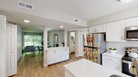 This well-appointed single-floor residence offers a thoughtfully designed layout that balances functionality and comfort throughout. The kitchen serves as a central hub of the home, featuring white shaker-style cabinetry, quartz countertops, a peninsula with an undermount sink, stainless steel appliances including a refrigerator, microwave, and electric range, and a subway tile backsplash. Light wood-look flooring runs through the kitchen and connecting areas, adding warmth to the clean, modern aesthetic. The kitchen opens seamlessly toward the living area, which is anchored by large sliding glass doors that flood the space with natural light and offer serene views of lush greenery outside. The living room provides a relaxed, airy atmosphere enhanced by neutral tones and an open feel. The bedrooms are carpeted for comfort, each featuring neutral walls, generous closet space with bifold doors, and windows that frame verdant outdoor views, contributing to a calm and restful environment. The bathroom is finished with wood-look flooring, a walk-in glass-enclosed shower with tile surround, and clean, minimalist fixtures. Throughout the residence, a consistent palette of soft neutrals, white cabinetry, and natural light creates a cohesive and inviting ambiance.